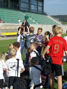 Schüler freuen sich über das gewonnene Fußballturnier und halten einen Pokal hoch.